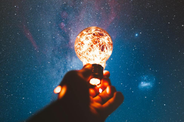 person holding a lightbulb to the night sky