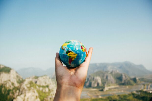 person holding small globe in hand with mountains in background