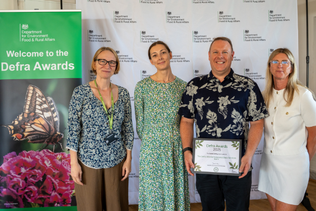 4 People stood in front of a 'welcome to the Defra awards' banner holding their framed award certificate